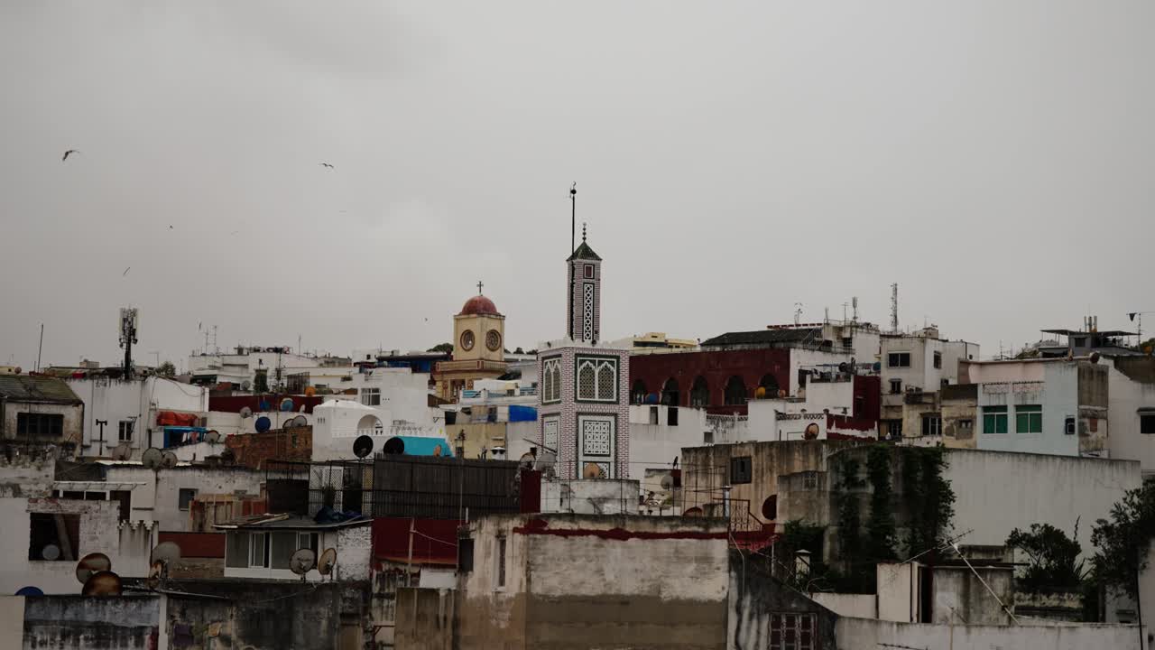 Vista dal tetto della medina di Tangeri con minareto di moschea e cupola di chiesa sotto un cielo nuvoloso.