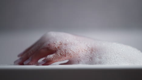 mujer espumosa mano manicurada mano toca el borde de la bañera primer plano. dama disfruta de procedimientos de belleza bañarse con mousse en el baño de casa. relajación y lavado del cuerpo