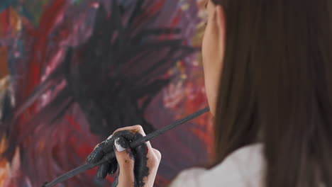 artist holds brush looking at canvas with abstract drawing