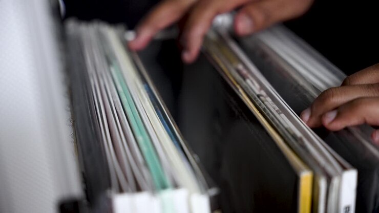 A close-up shows hands sorting through vinyl records in a collection