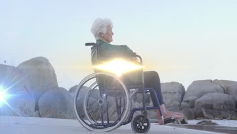 Animación-De-Luz-Moviéndose-Sobre-Una-Mujer-Caucásica-Mayor-Sonriente-En-Silla-De-Ruedas-En-La-Playa-Mirando-Al-Mar