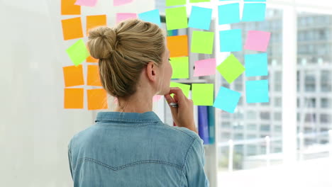 blonde designer looking at post its on window