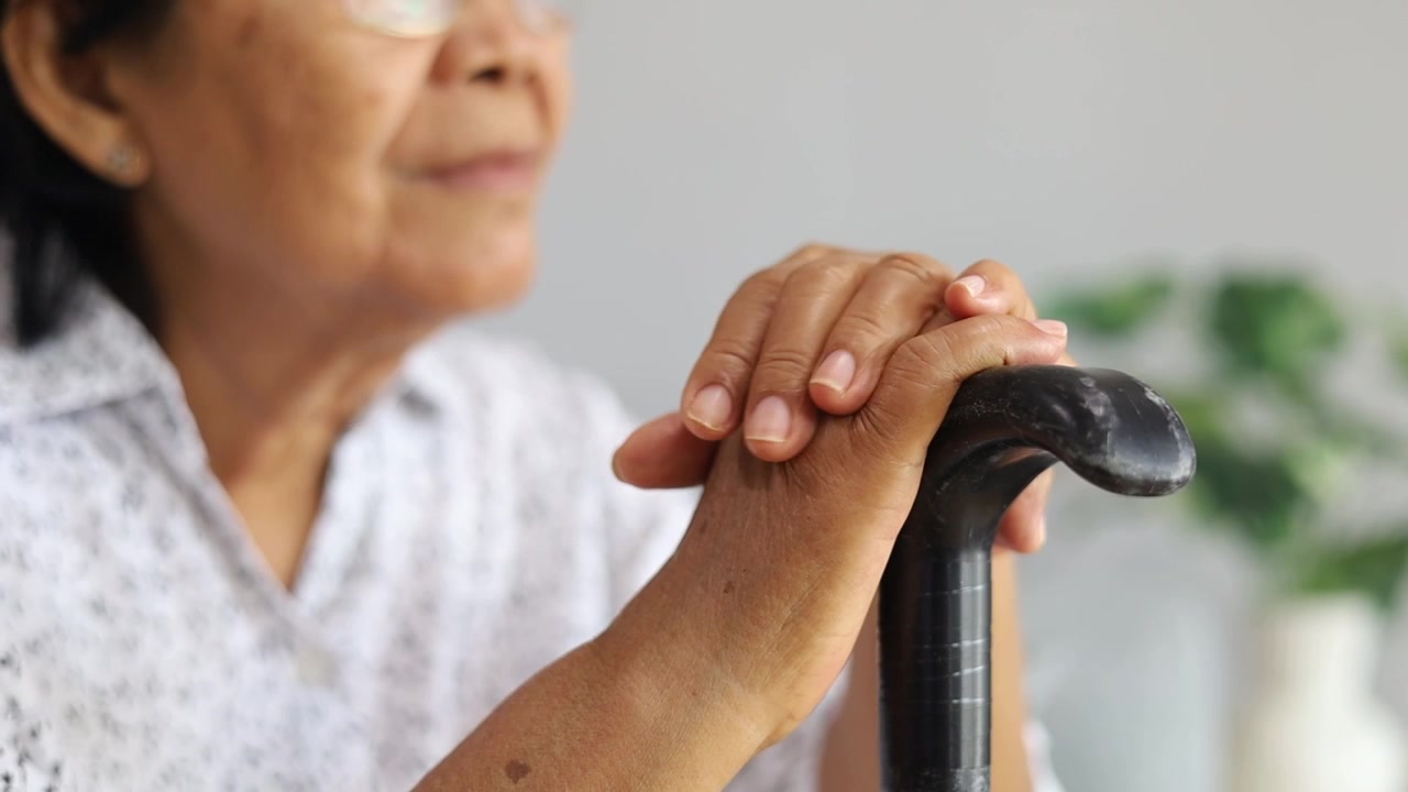Primo piano della mano di una donna asiatica disabile che tiene un bastone da passeggio, si sente sola e soffre di solitudine, affetta da disturbo del movimento (morbo di Parkinson), concetto fisico.