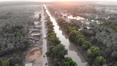 Morgendlicher-Sonnenaufgang-Aus-Der-Luft-über-Wasserstraße-Und-Straße,-Umgeben-Von-Dattelfarmhain-In-Khairpur-Sindh-Pakistan