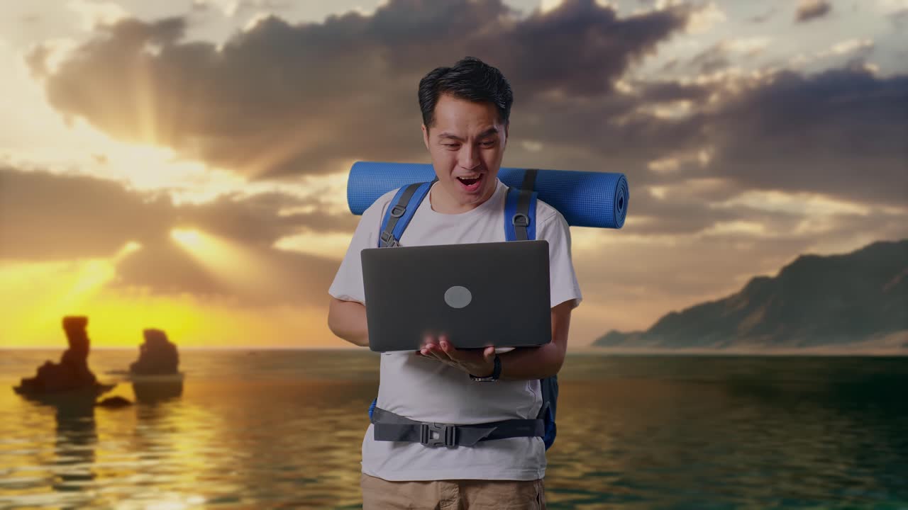 Aziatische mannelijke wandelaar met bergbeklimmersrugzak die op een strand naar een laptop kijkt en wow zegt