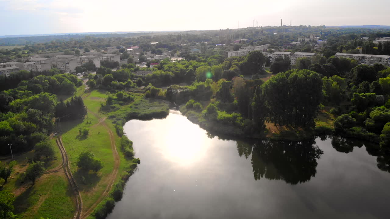 Aerial drone shot of Donduseni city with multiple residential buildings and greenery. Park with a lake on the foreground. Sunset in Moldova