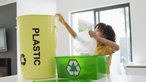 happy biracial boy sorting plastic bottles and waste in kitchen