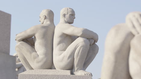 a pair of strong granite men sit back to back next to the monolith, vigeland