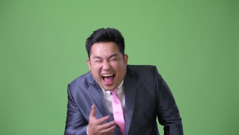 young handsome overweight asian businessman against green background