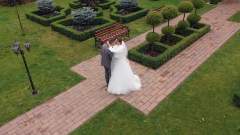 Newlyweds,-bride-embracing-groom-in-park-making-kiss,-wedding-couple-family-hugging,-aerial-view