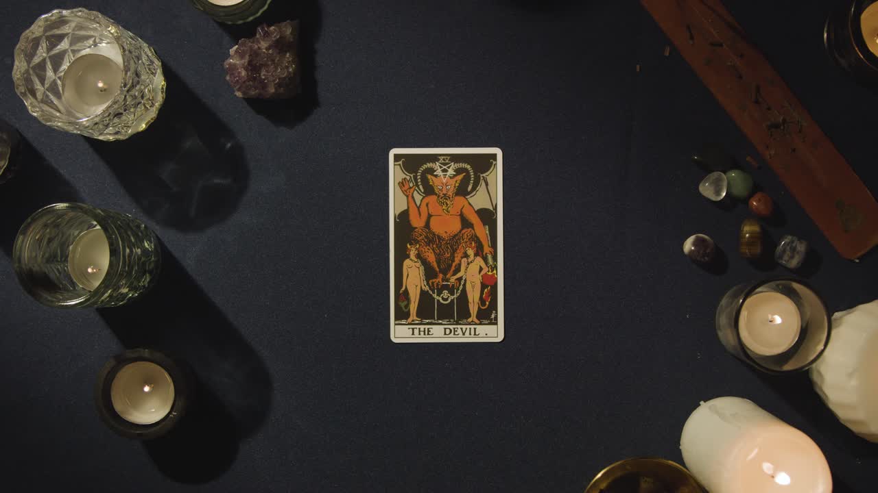 disparo de arriba de una persona que da la lectura de la tarjeta del tarot colocando la tarjeta del diablo en la mesa