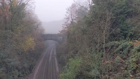 Vías-De-Tren-Brumosas-De-Niebla-Que-Conducen-Al-Túnel-Con-Bosque-Circundante-Uk-4k