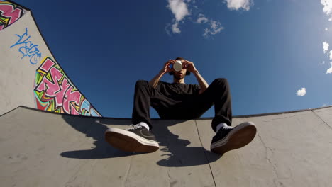 man relaxing with coffee and headphones at a skate park