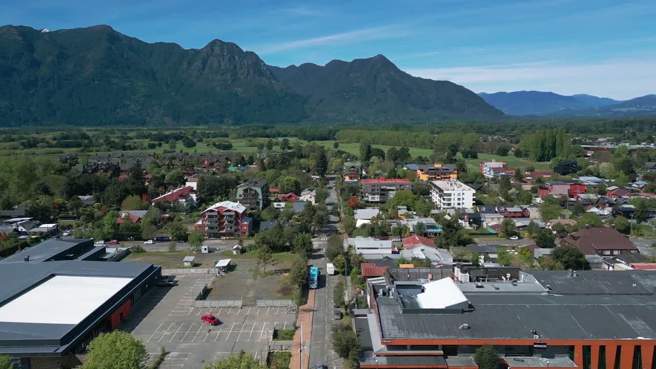 Aerial view of Pucón, Chile, showing colorful rooftops, modern buildings, and mountains under a clear blue sky