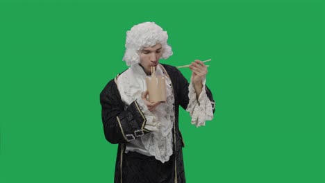 portrait of courtier gentleman in black vintage suit and wig, enjoying chinese noodles using chopsticks. young man posing in studio with green screen background. close up. slow motion ready 59.94fps