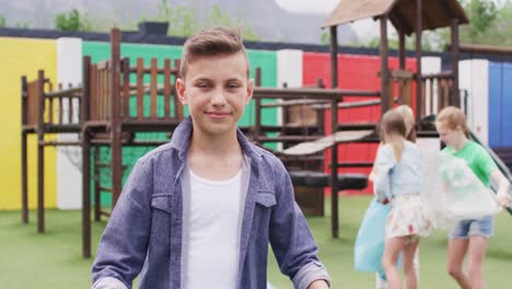 portrait of happy caucasian schoolchildren cleaning with bags at school playground