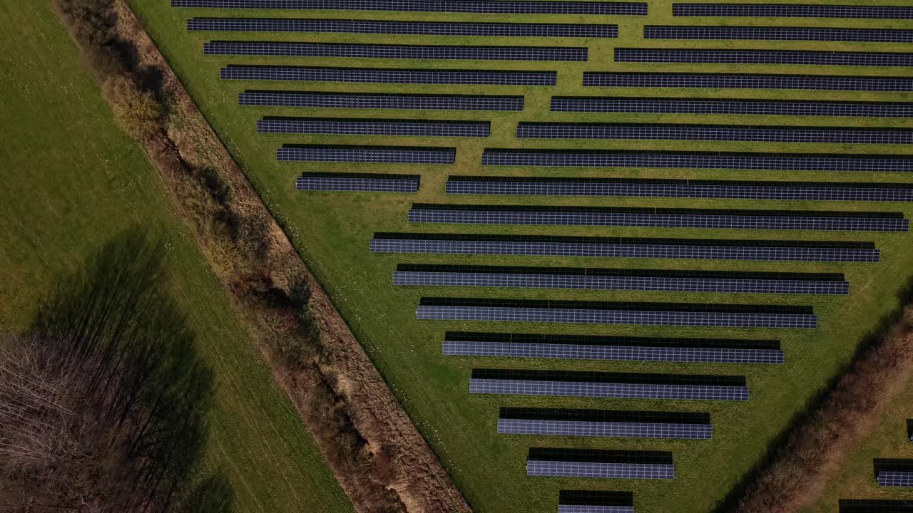 Luftfoto i tilt-op af stor solcellepark langs motorvej i USA, viser rækker af solcelleanlæg i grønt landskab. Moderne scene med vedvarende energi med forbikørende biler og bæredygtig energiproduktion