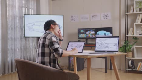 side view of asian male yawning while drawing new car design concept on a tablet in the studio with tv and computers display 3d electric car model