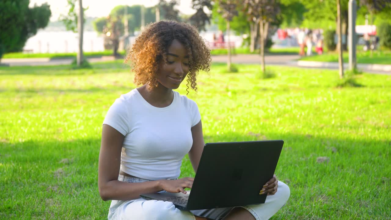 joven afroamericana usando una computadora portátil en el parque. concepto de trabajo remoto