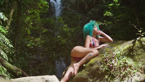 a woman laying on a rock in a bikini with a flowing waterfall in the background