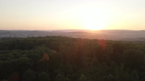 Imágenes-De-Drones-En-Aumento-Sobre-Un-Enorme-Bosque-En-Una-Puesta-De-Sol-Naranja-Con-Montañas-En-El-Fondo