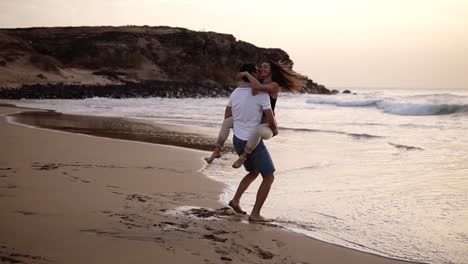 Couple-in-love.-Man-in-shirts-turning-around-his-lovely-woman-on-beach-and-sensually-kissing.-Full-length-view-of-happy-young-barefoot-man-and-woman-having-fun-together-on-sandy-beach