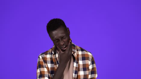 Portrait-of-sick-african-american-man-in-plaid-shirt-touching-jawbone-with-pain-on-face-and-suffering-from-dental-problem,-isolated-over-blue-background.-Concept-of-emotions