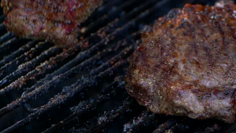 a fork turns a nearly cooked juicy rib eye steak on a grill as blood drips from it in slow motion