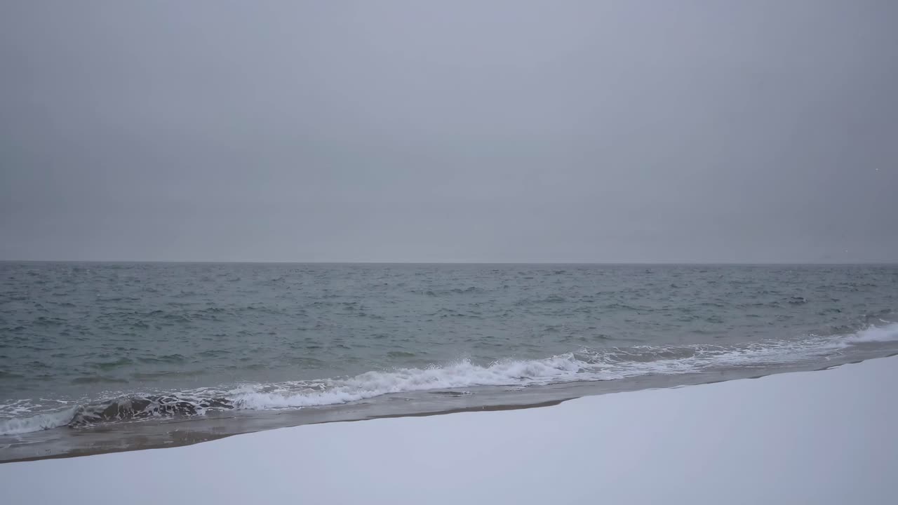 A serene, wide-angle video shot of a calm beach with gentle waves under a cloudy sky