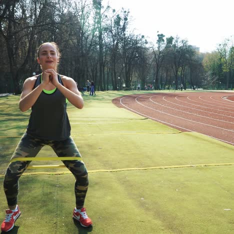 woman doing exercises outdoors at the stadium. beautiful young woman working with elastic band. fitness concept.