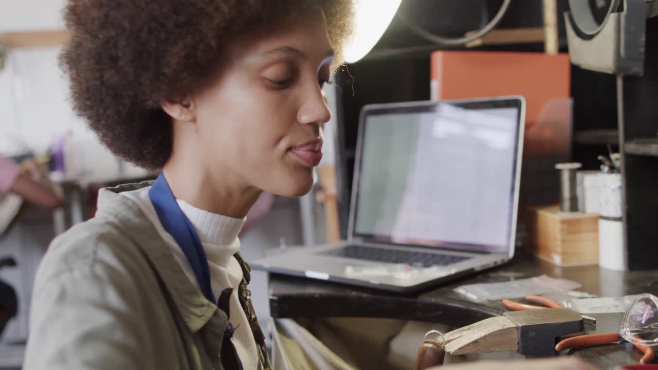 Busy biracial female worker with laptop shaping jewellery in studio in slow motion