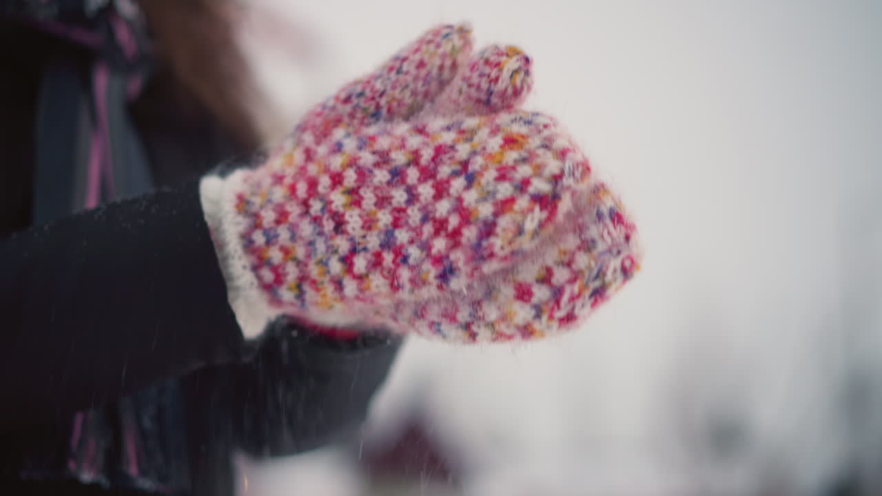 Closeup of colorful knitted mittens clapping together outdoors in cold winter air, snow particles scattering in motion, creating cozy seasonal moment with warmth, color and festive holiday atmosphere