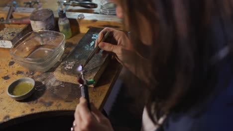 close up of caucasian female jeweller sitting at desk, making jewelry in workshop