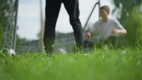 a close-up of a leg kicking a soccer ball into the goalpost, the goalkeeper, positioned in the background, misses the save