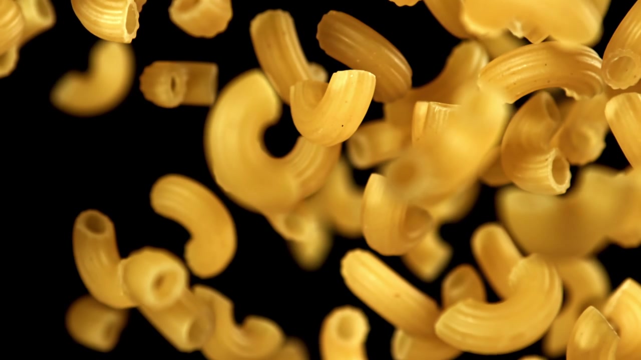 Maccheroni secchi che cadono al rallentatore su uno sfondo nero.