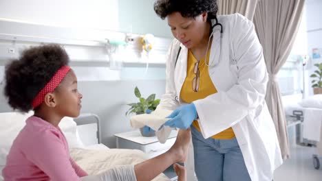 Afroamerikanische-Ärztin,-Die-Im-Krankenhauszimmer-Einen-Verband-Am-Bein-Eines-Mädchens-Anlegt,-Zeitlupe