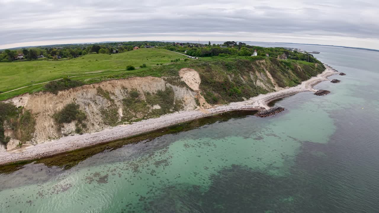 Aerial drone view of a rugged coastal cliff with green fields above and clear turquoise waters below on a bright day