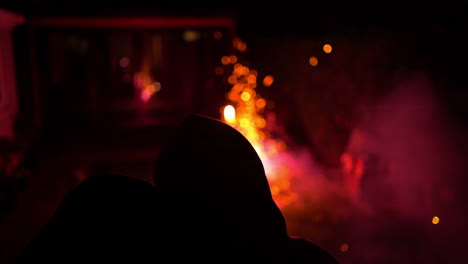 Fireworks-in-yard-young-couple-wearing-hoodies-hug-silhouette-against-bright-colours-sparks-and-flares