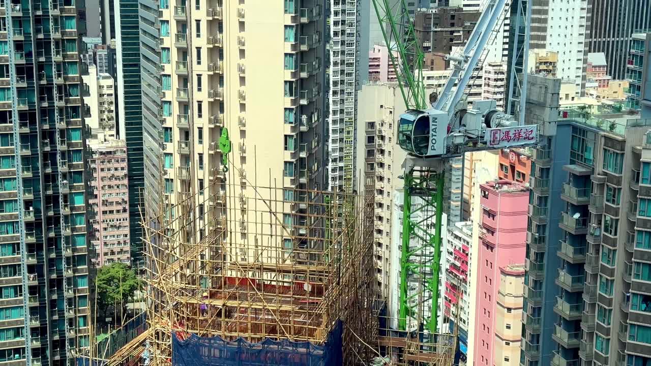sitio de construcción con andamios de bambú en el denso paisaje urbano de hong kong con edificios residenciales de gran altura circundantes y grúa torre
