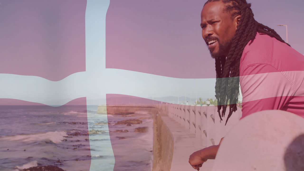 Standing by ocean with Danish flag overlay, man with long hair
