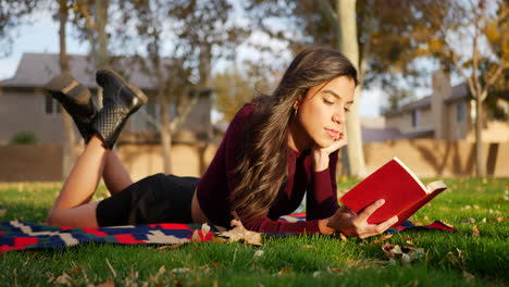 attractive young hispanic woman college student reading a book outdoors in the park before class starts in the fall semester