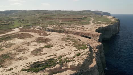 Aerial-reveal-shot-of-majestic-cliffs-and-a-limestone-arch-called-Wied-il-Mielaħ-on-the-island-of-Gozo,-Malta---Mediterranean-travel-destination