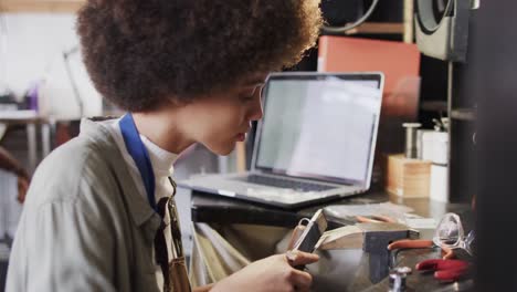 busy biracial female worker with laptop shaping jewellery in studio in slow motion