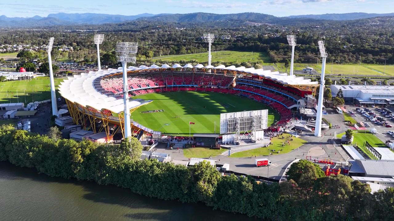 High-angle drone shot of a large sports arena under bright sunlight with green landscape.