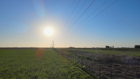 Flight-along-fence-on-farm-with-overhead-power-lines,-the-Pampas-region,-aerial