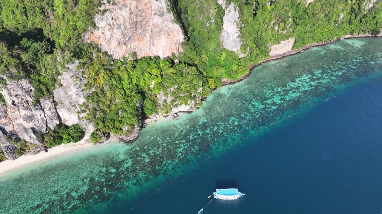 Steep limestone cliff with small beach coral reef, crystal clear water. Koh Phi Phi Islands, Thailand, drone