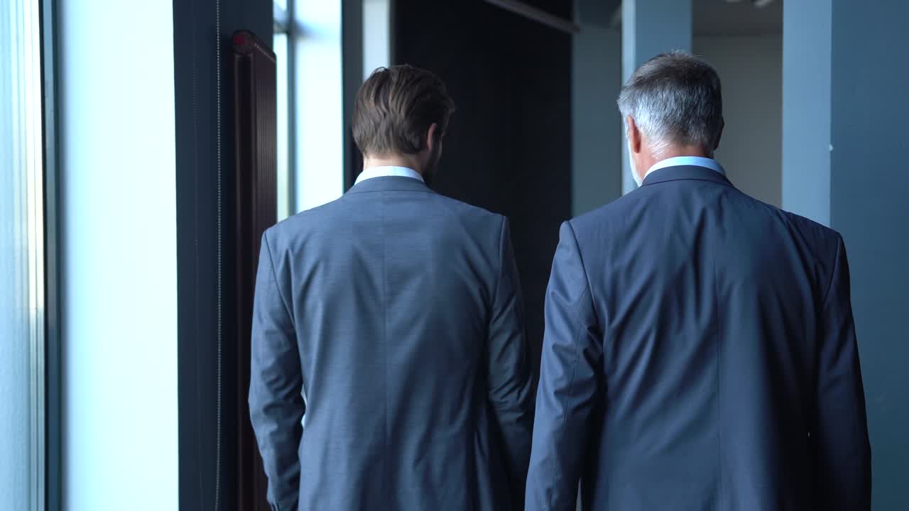 Rear view of business executives meeting in modern corporate office lobby, walking and talking.