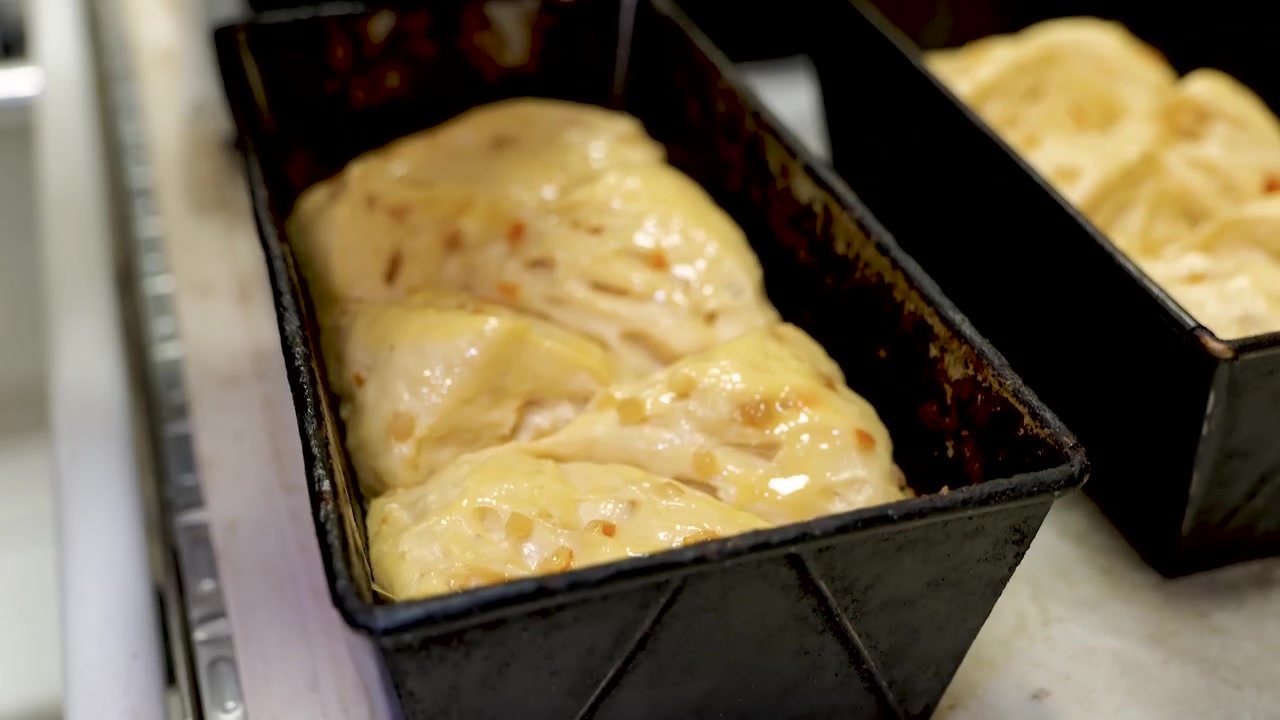 A baker's hand brushes egg wash onto brioche loaves with a pastry brush.