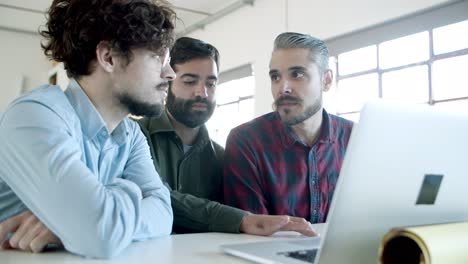 Concentrated-young-people-sitting-at-table-and-looking-at-laptop