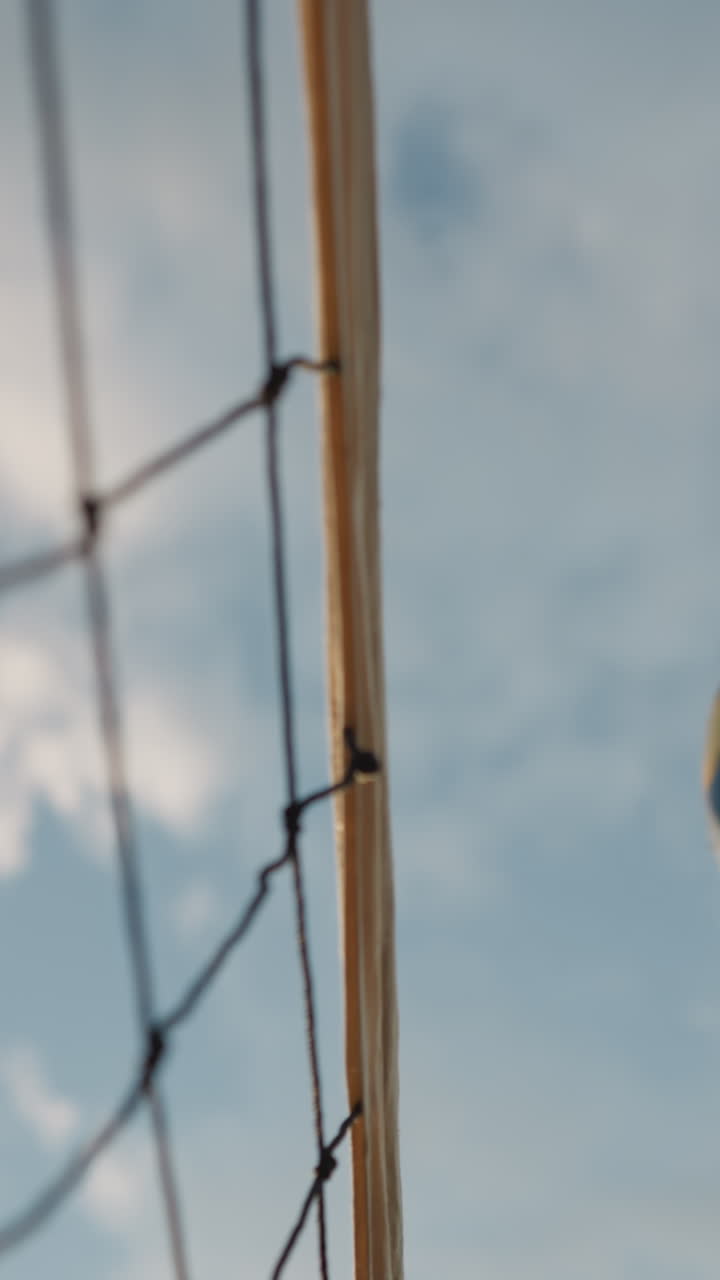 밝은 파란 하늘을 배경으로 공이 날아가는 배구 네트의 동적 근접 촬영, 야외 배구 경기의 액션 한 순간을 포착하여 움직임을 강조합니다.